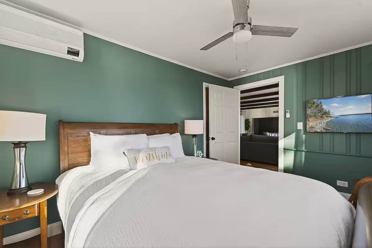 Bright bedroom with white bed, green walls, ceiling fan, and open door to bathroom