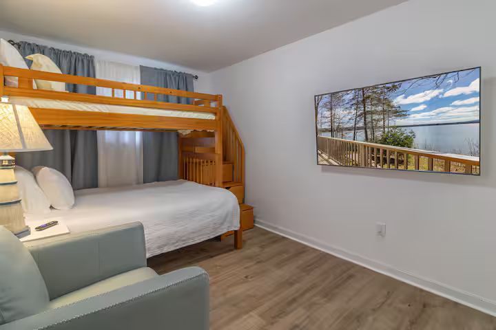 Bright bedroom with wooden bunk bed, white bedding, armchair, and beach landscape wall art.