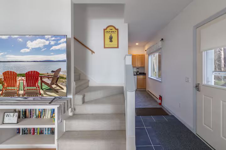 Bright entryway with stairs, coat hook, hallway, and beach-themed TV on a shelf