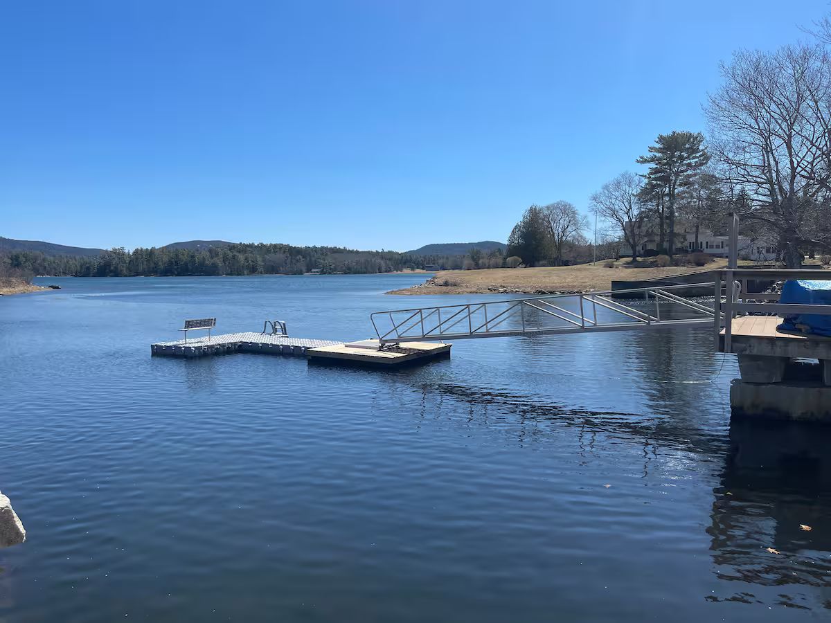 Quiet lake with floating dock, clear blue water, and trees along the shore under a bright sky.