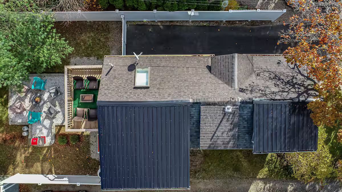 Aerial view of a house with gray roof, dark blue awnings, and a small backyard by a street.