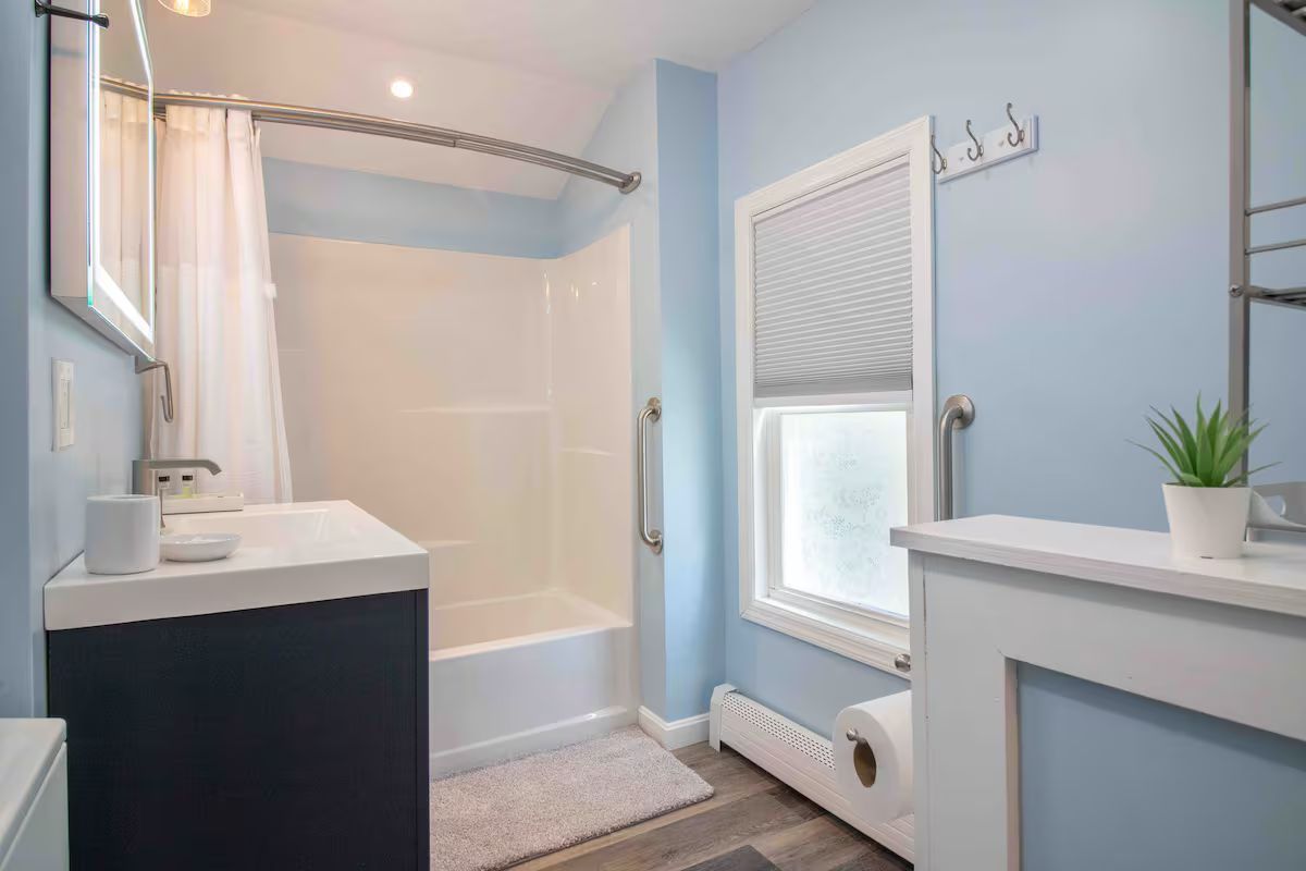 Bright bathroom with a white tub, light blue walls, sink vanity, window, and radiator