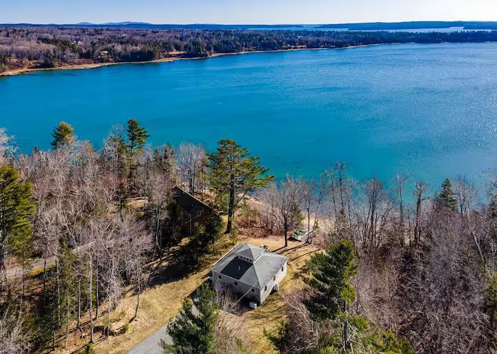 Aerial view of a lakeside cabin surrounded by leafless trees and blue water