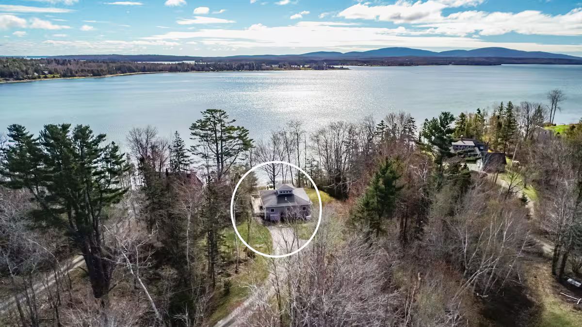 Aerial view of a lakeside wooded area with a small house and a large body of water in the background