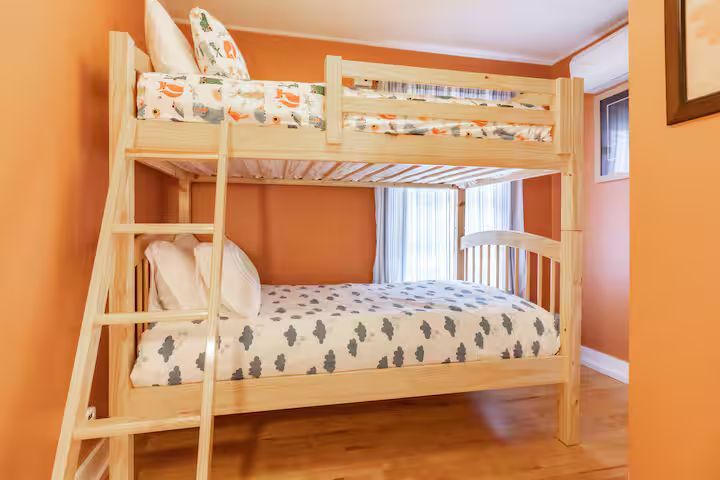 Wooden bunk bed with patterned bedding in a warm orange bedroom.