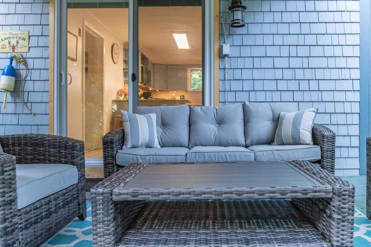 Wicker patio sofa and coffee table on a covered porch with sliding glass doors and light blue siding