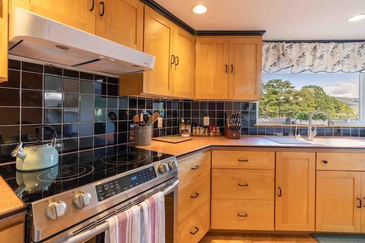 Bright kitchen with wood cabinets, black tile backsplash, stove, sink, and window view