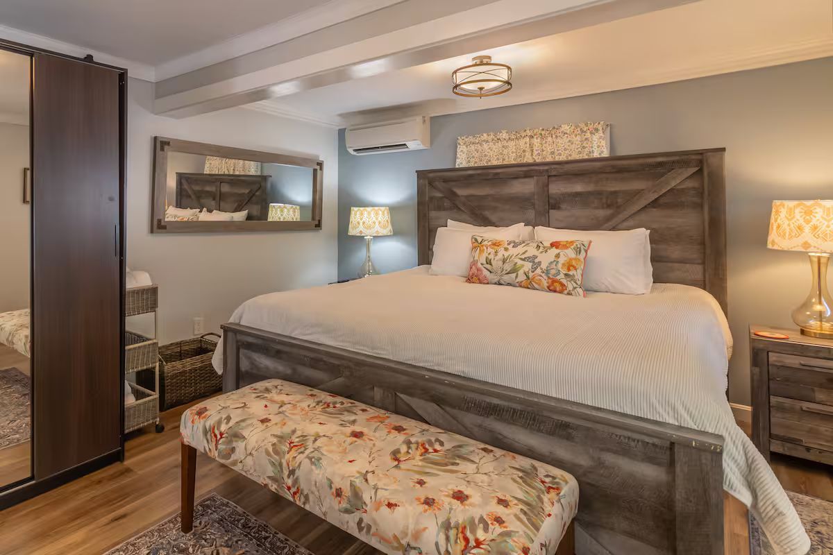 Cozy bedroom with a gray upholstered bed, floral bench, nightstands, and warm lamp lighting