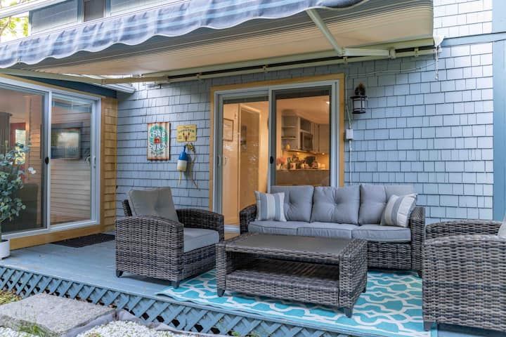 Back patio with wicker seating, blue rug, and glass doors under a striped awning