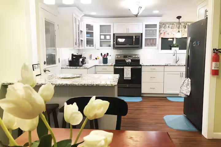 Bright kitchen with white cabinets, black appliances, wood floors, and a dining table with tulips in the foreground