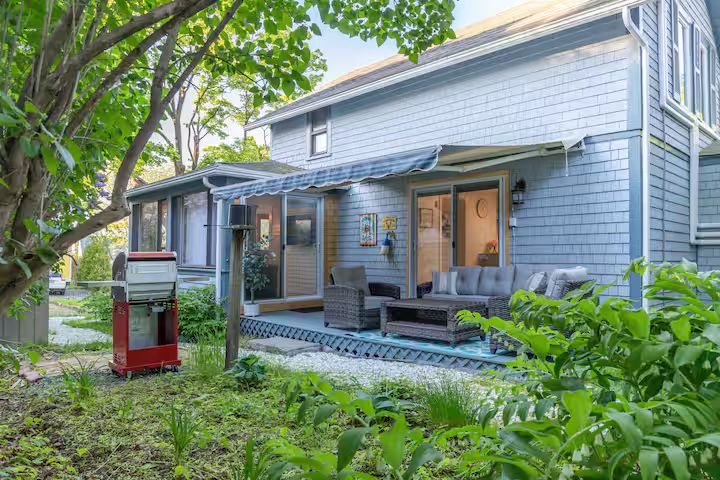 Blue two-story house with a small porch, large windows, and lush greenery in the yard