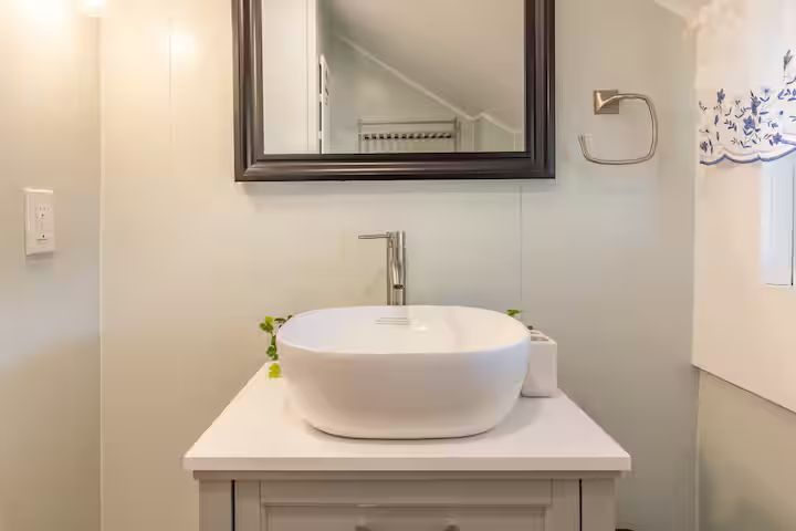 White bathroom vanity with round sink, mirror, and faucet in a bright, modern restroom