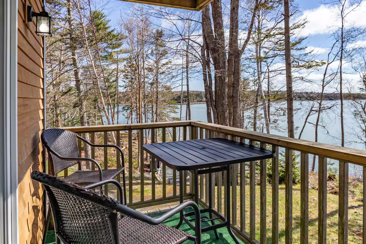 Wooden porch with black chairs and table overlooking a lake through pine trees