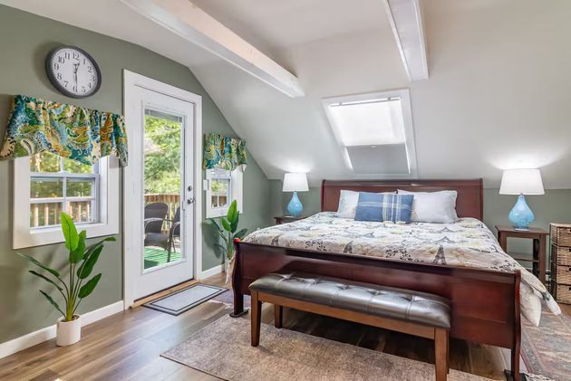 Bright bedroom with a wooden bed, bench, skylight, and sliding glass door to a sunny patio