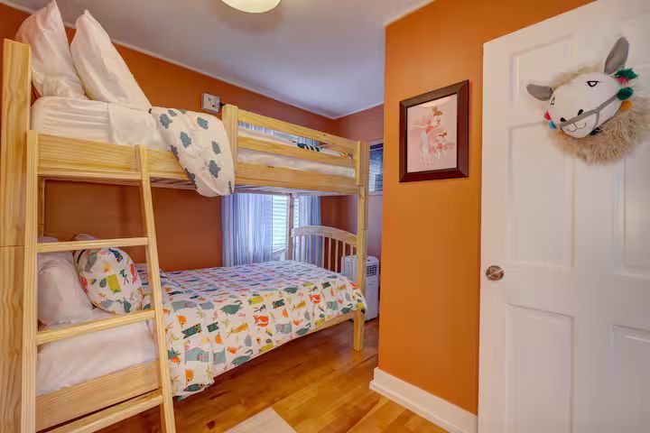 Children’s bunk bed room with orange walls, white door, and colorful bedding