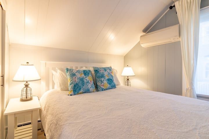 Cozy white bedroom with a large bed, blue pillows, and soft bedside lamps