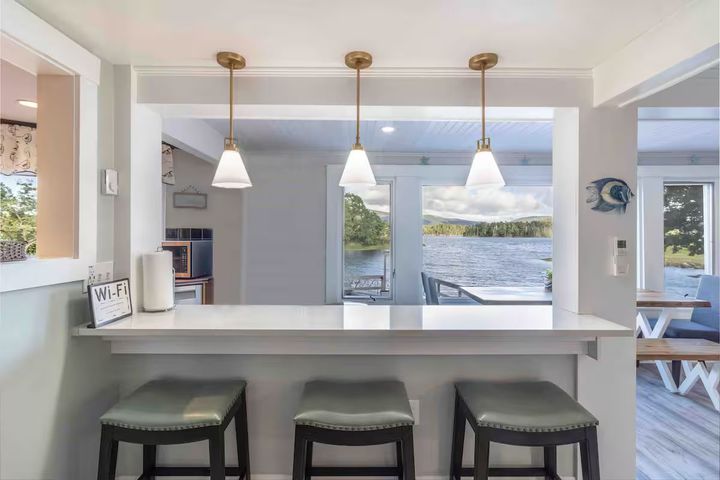 Bright kitchen bar with three stools overlooking a lake through large windows