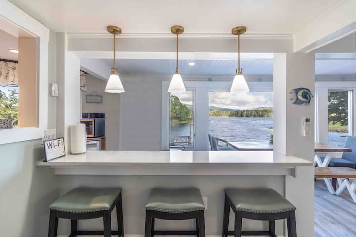Bright kitchen breakfast bar with stools, pendant lights, and a lake view through large windows