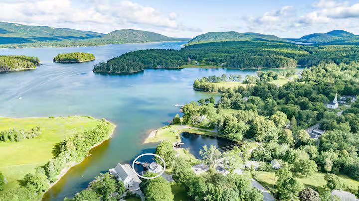Aerial view of a blue lake with green islands, forested shores, and rolling hills under a clear sky