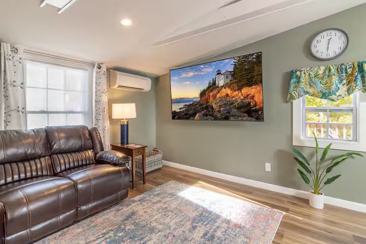 Bright living room with leather sofa, wall art, lamp, window, clock, and potted plant on wood floors