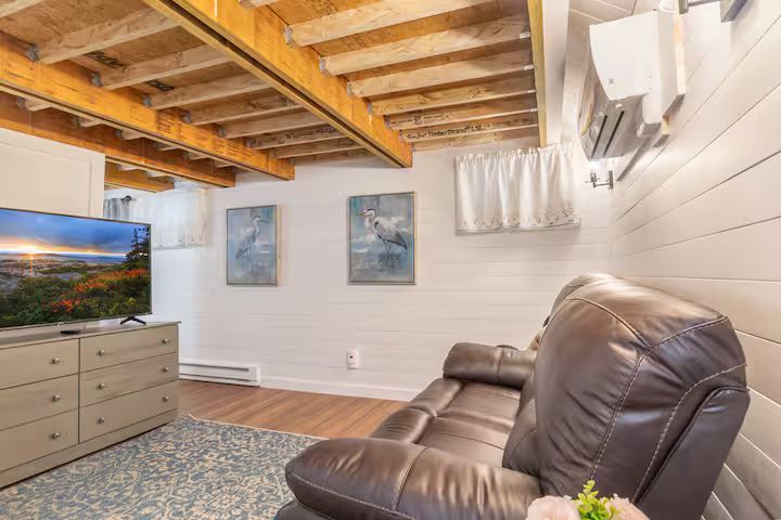 Living room with leather recliner, dresser, wall art, TV, and exposed ceiling beams