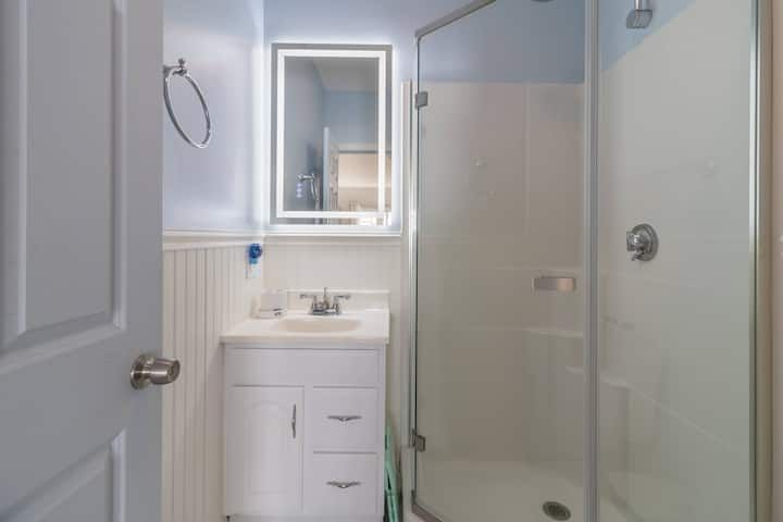 Small white bathroom with vanity sink, mirror, and glass shower stall