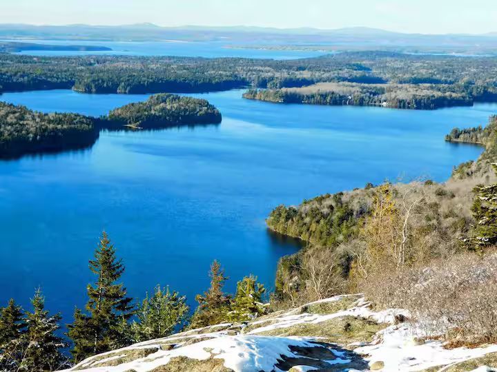 Blue lake with forested islands and snowy shoreline under a clear sky