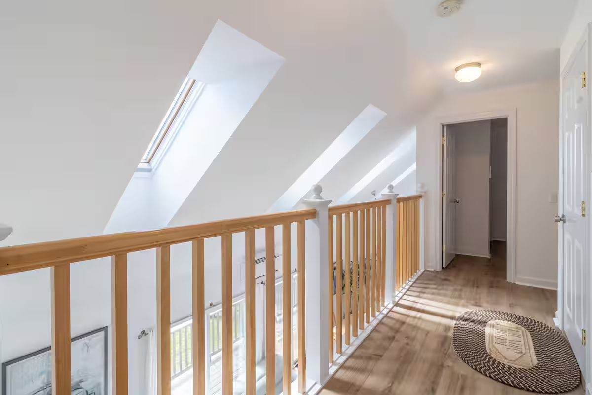 Bright upstairs hallway with skylight windows, wooden railing, and a doorway at the end