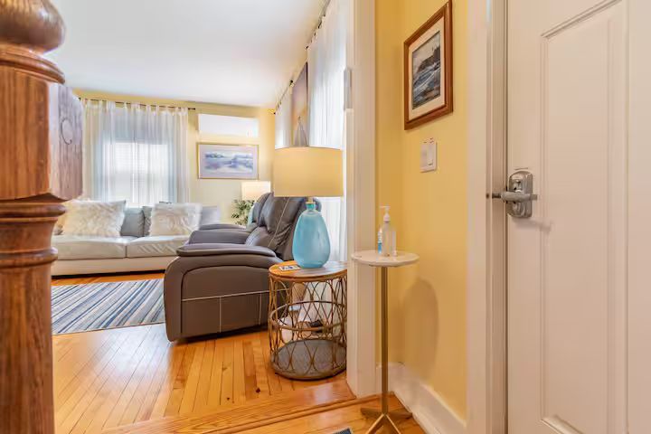 Bright hallway opening to a cozy living room with gray sofa, lamp, and hardwood floors