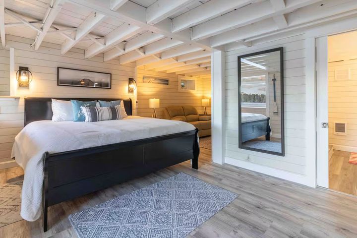 Bright bedroom with exposed white beams, black bed, patterned rug, and a full-length mirror near the door