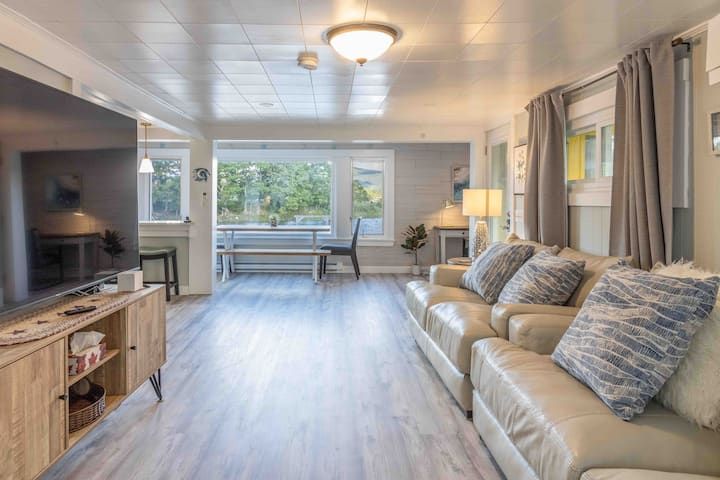 Bright living room with beige sofa, TV, large windows, and light wood flooring