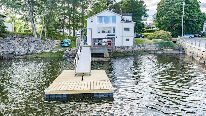 Floating dock with a white ramp leading to a lakeside house, surrounded by rippling water and trees
