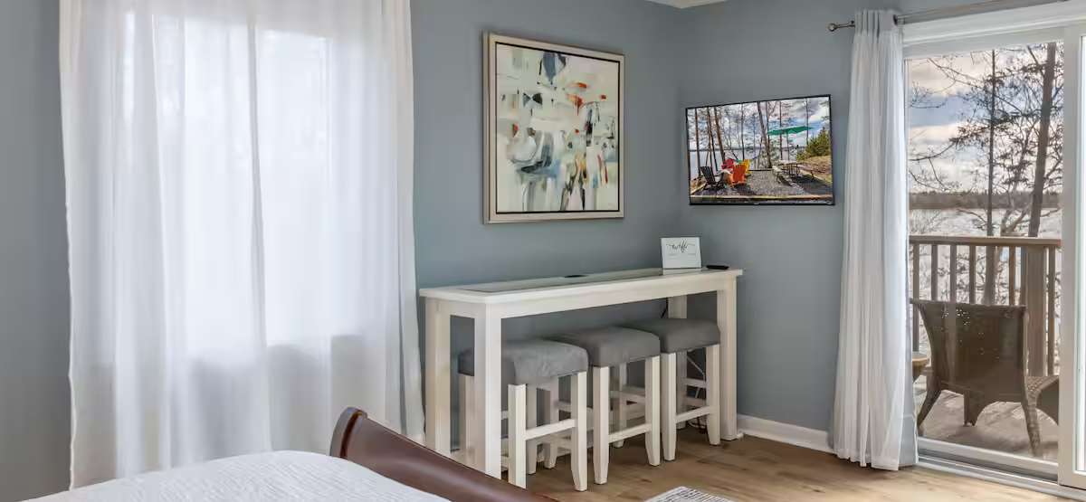 Bright bedroom corner with white curtains, desk, stools, and balcony doors overlooking snowy trees