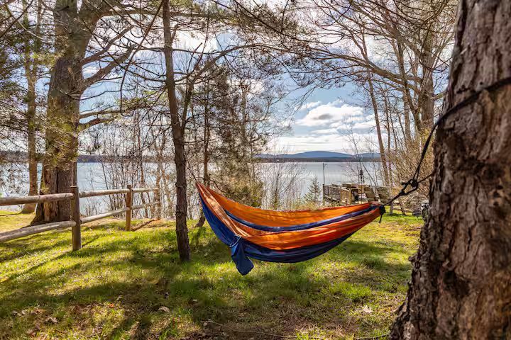 Orange and blue hammock strung between trees beside a calm lake on a sunny day