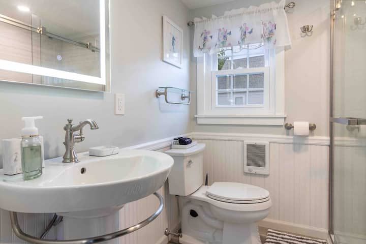 Small white bathroom with sink, toilet, window, mirror, and towel rack