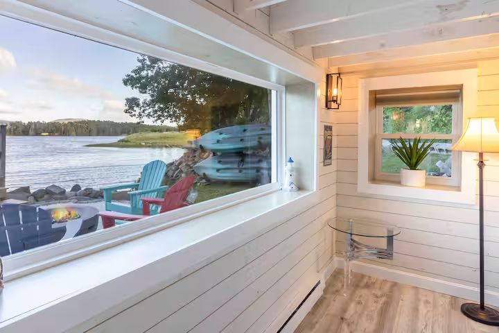 Cozy white porch with water view, Adirondack chairs, a small boat, and a lit floor lamp