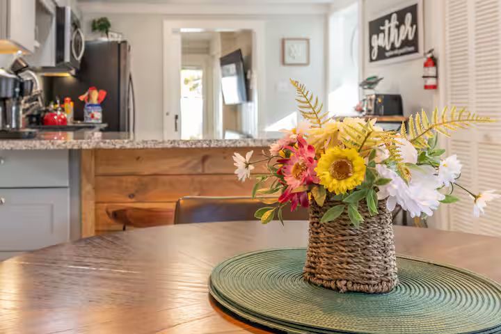 Kitchen table with wicker floral centerpiece in front of a bright, modern kitchen.