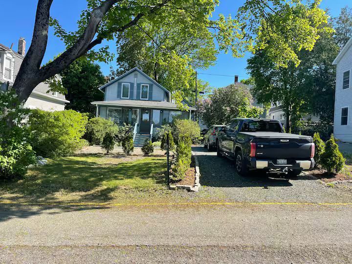 House with front porch and driveway, black pickup truck parked in front, surrounded by trees and greenery