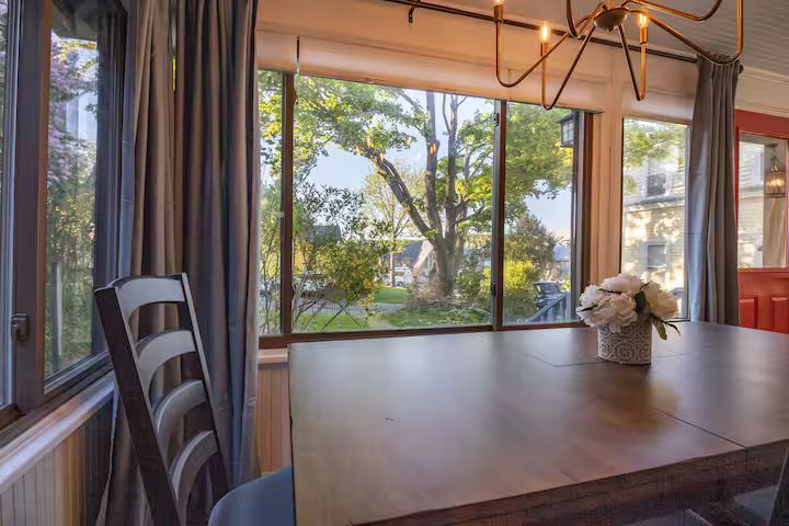 Dining table by large windows overlooking a green garden, with a chair and flowers in a bright room