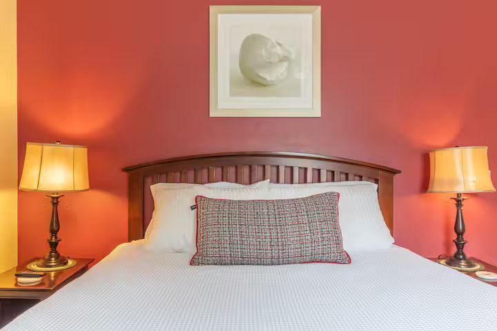 Red bedroom with a wooden bed, white bedding, two lit lamps, and framed wall art.