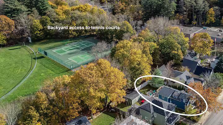 Aerial view of a green sports field and nearby houses surrounded by autumn trees, with one house circled in white.