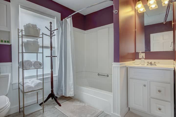 Bathroom with white tub, vanity, shower curtain, and coat rack on tiled floor with purple walls