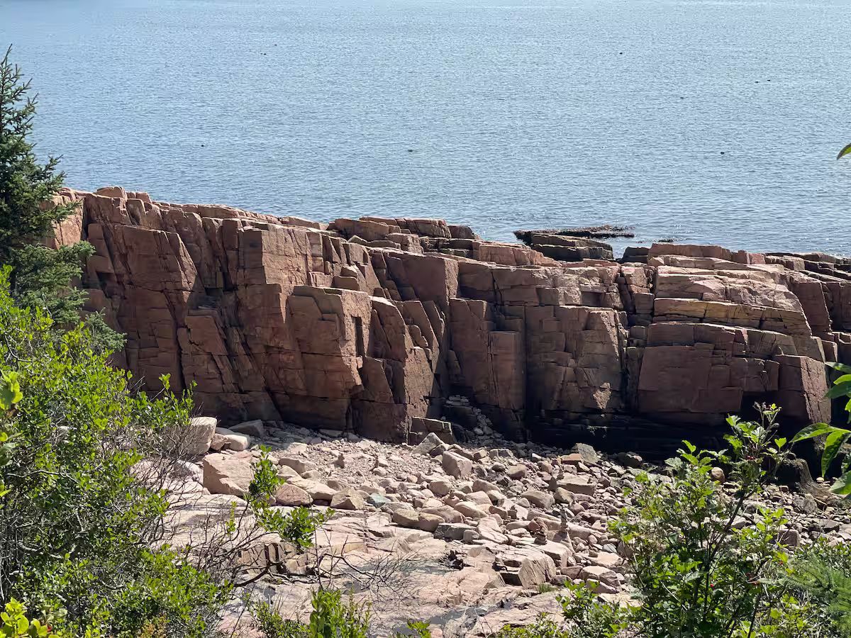 Rocky seaside cliff with calm blue water and sparse green shrubs in the foreground
