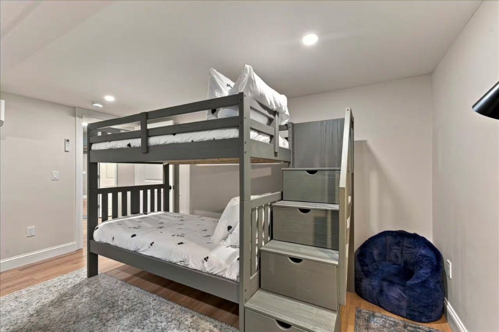 Gray bunk bed in a minimalist bedroom with white walls, gray rug, and blue bean bag chair