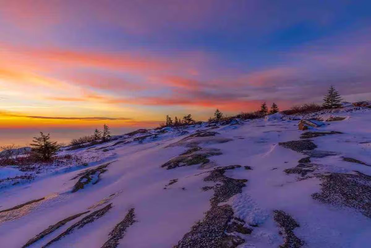 Snow-covered hillside at sunset with pink and purple sky over a distant horizon
