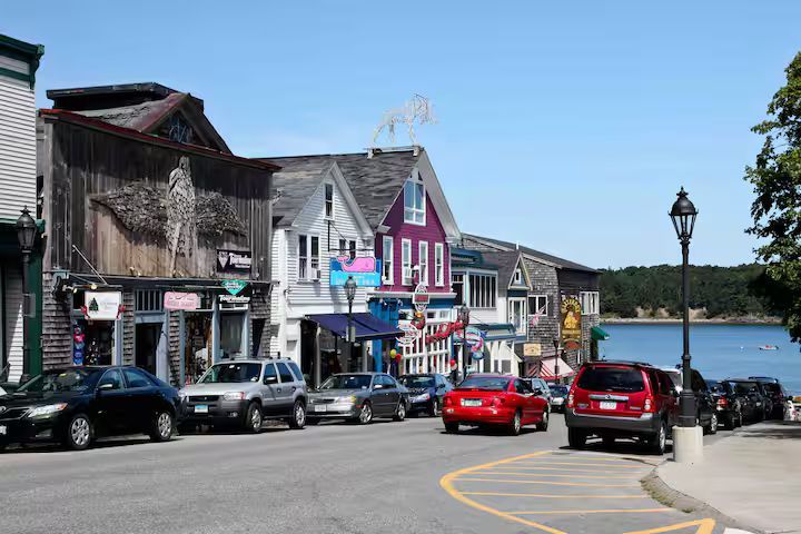 Colorful waterfront street with shops, parked cars, and a red SUV on a sunny day