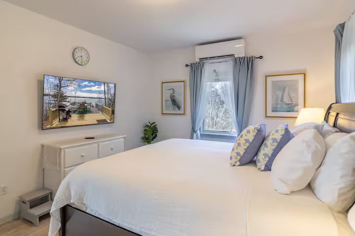 Bright bedroom with a large white bed, blue accents, wall art, and a window with gray curtains