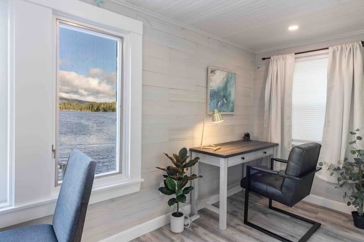 Bright home office with desk, chair, plants, and a large window overlooking water
