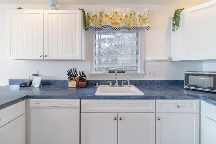 White kitchen with blue countertops, sink under a window, cabinets, and a microwave on the right.