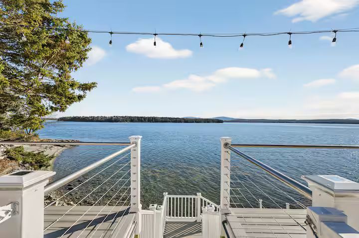 Deck overlooking calm blue water with string lights and a distant shoreline